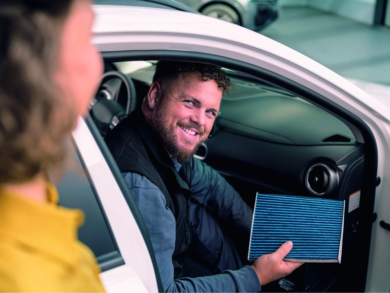 Mann der im Auto sitzt und einen Innenraumfilter in der Hand hält.